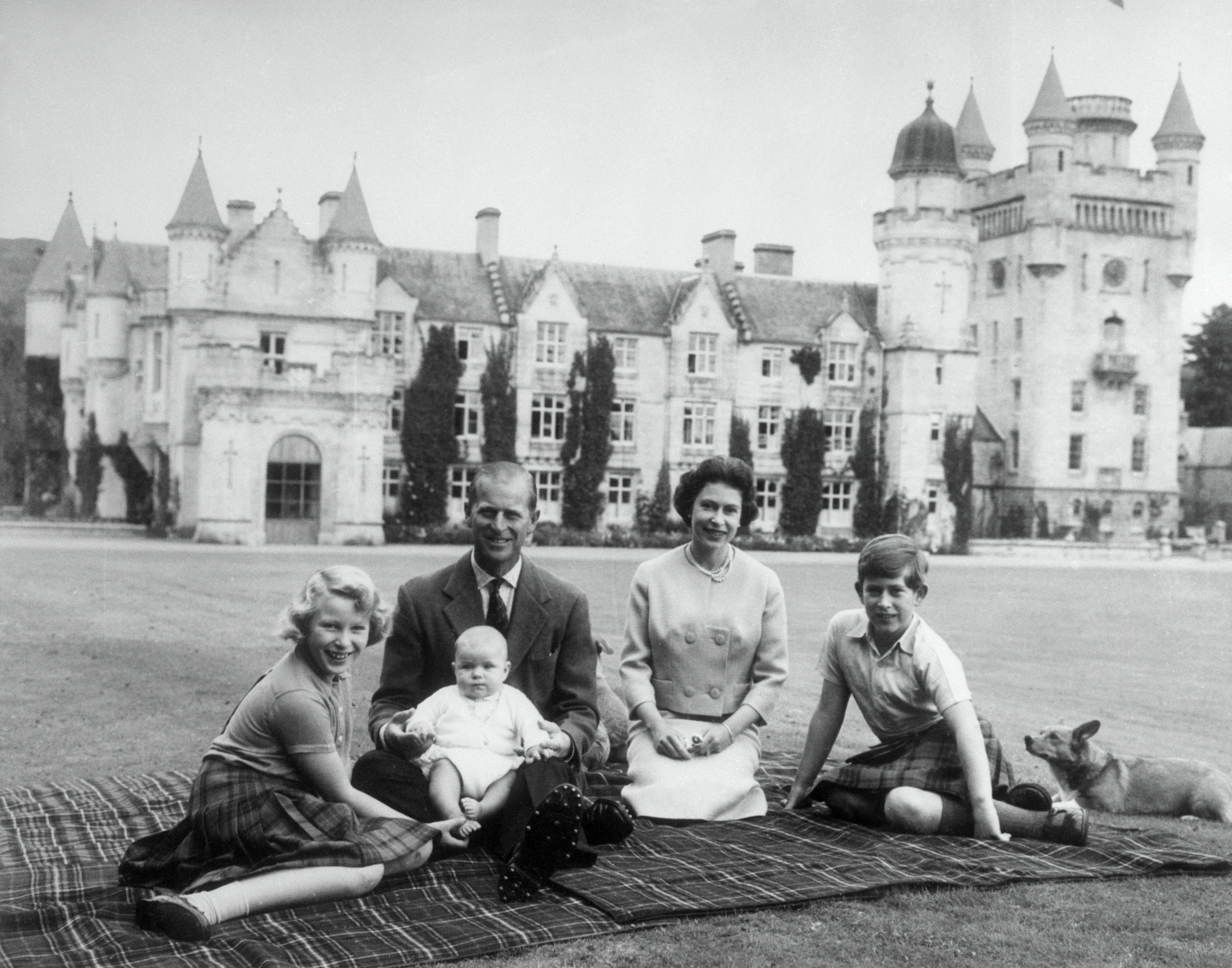 Prince Philip, Queen Elizabeth, Prince Andrew, Prince Charles and Princess Anne sitting on a blanket in front of Balmoral Castle