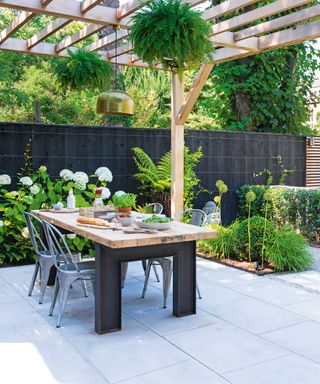a contmeporary patio with pale stone slabs and a wooden pergola with hanging ferns