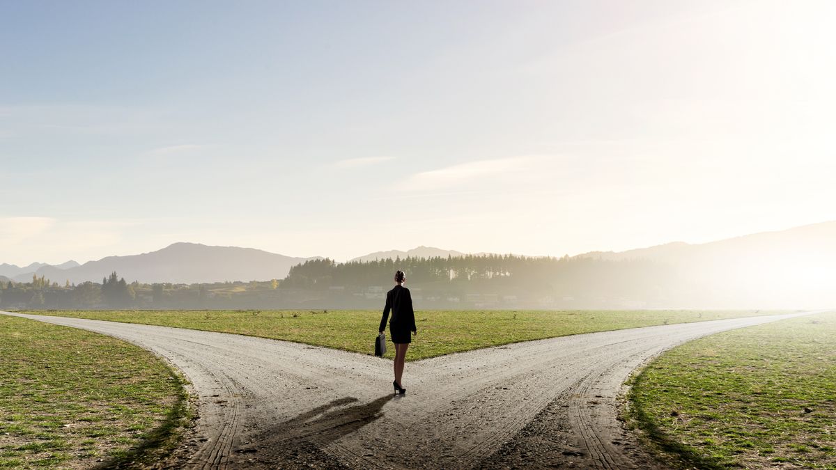 A business woman standing at a fork in the road, deciding which way to go