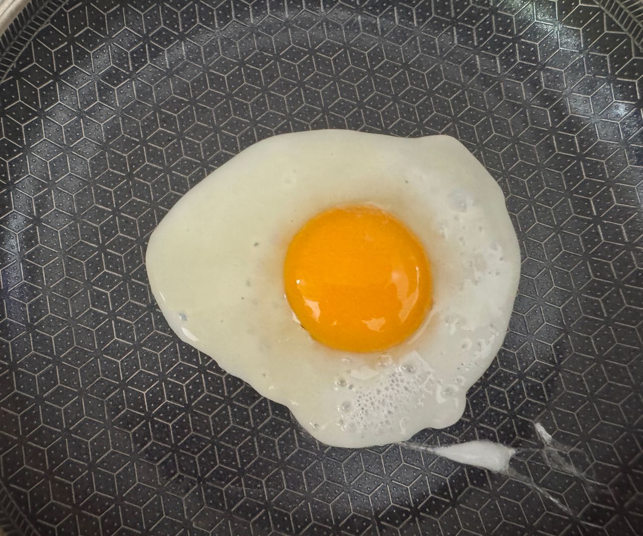 fried egg, sunny side up, in a black lined frying pan.