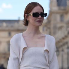 Emma Stone wearing an auburn straight bob hairstyle with black sunglasses and a cream dress outside Louis Vuitton during Paris Fashion Week Spring/Summer 2026
