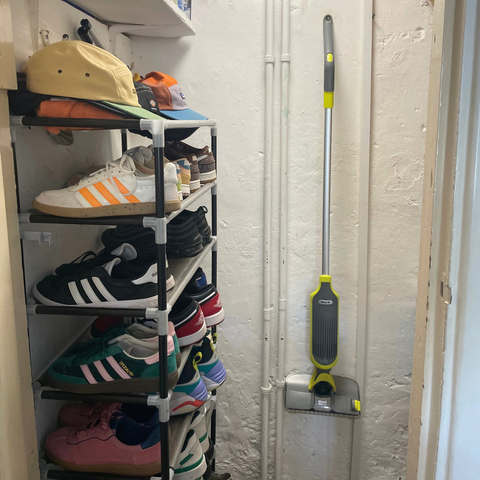 Shark VacMop hanging on the wall of an under the stairs cupboard next to a shoe rack