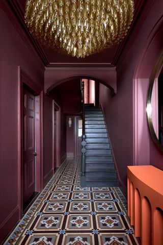 A burgundy hallway with patterned tiles and a black staircase