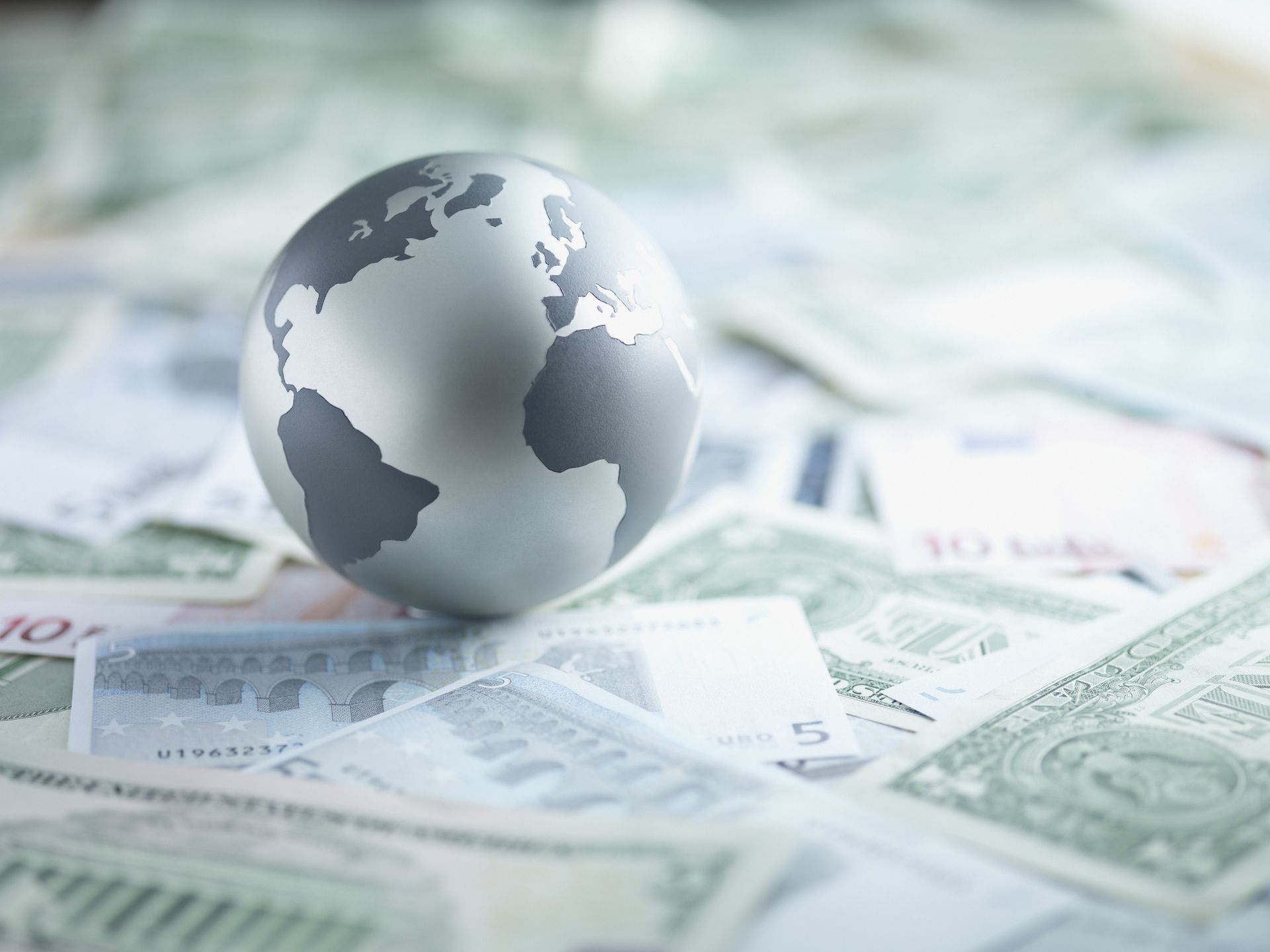 metal globe sitting on currencies from around the world