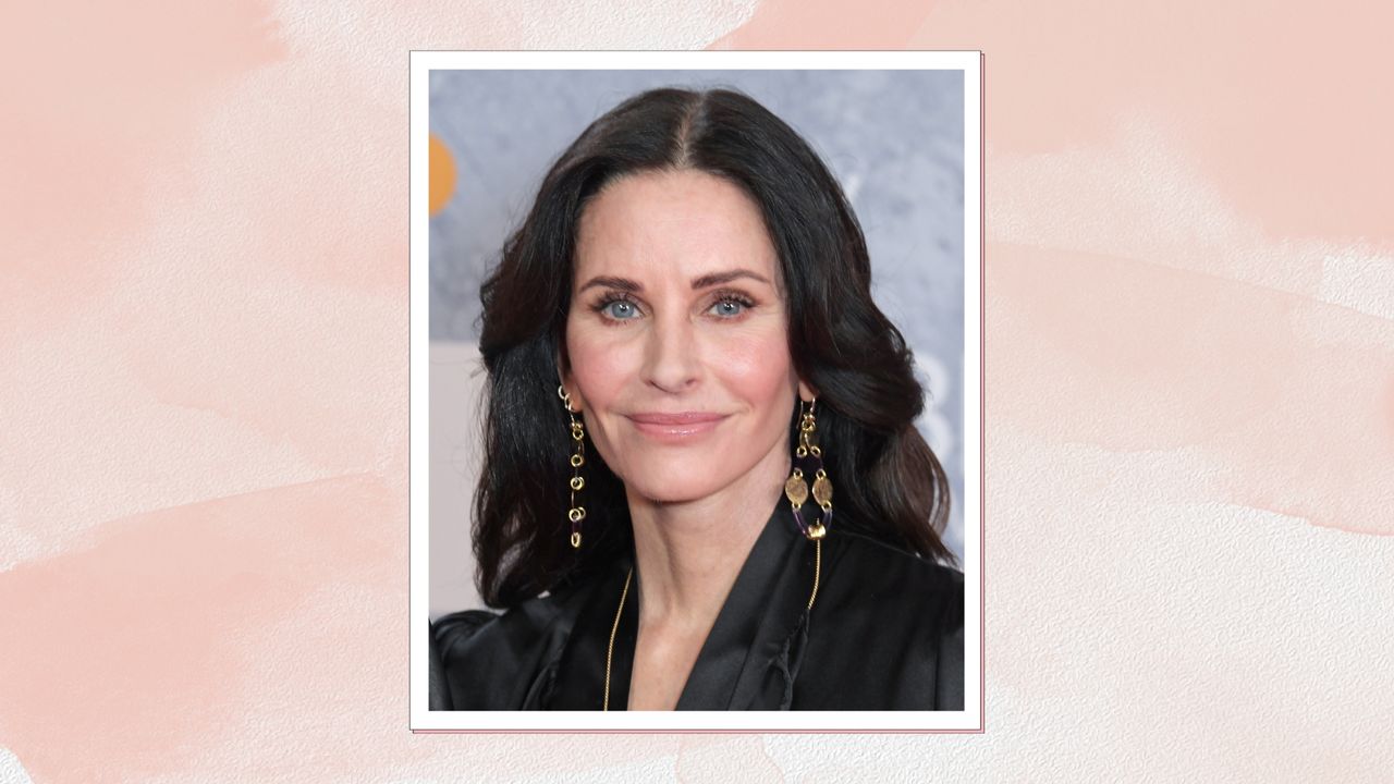 Courteney Cox is pictured with her hair in loose curls and wearing a black top at The BRIT Awards 2022 at The O2 Arena on February 8, 2022 in London, England/ in a pink watercolour paint-style template