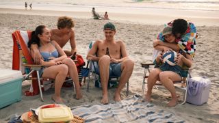 Belly (Lola Tung) sitting in a chair, Jeremiah (Gavin Casalegno) with his arm around Belly, Conrad (Christopher Briney) sitting in a chair holding beer, Steven (Sean Kaufman) standing over and hugging and Taylor (Rain Spencer) who is sitting in a chair. They are all at the beach.