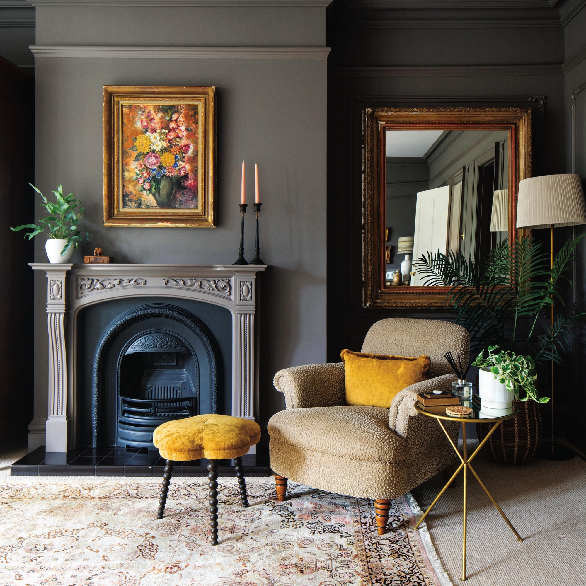 room with brown painted walls and fireplace with armchari, footstool and ornate mirror on the wall.