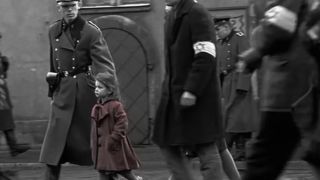 A little girl in a red dress stands out among a crowd in black and white in Schindler's List