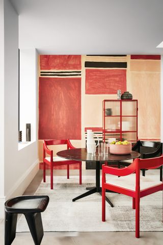 Dining room with red, plaster pink and black wall mural, neutral floor, black round dining table and bright red chairs