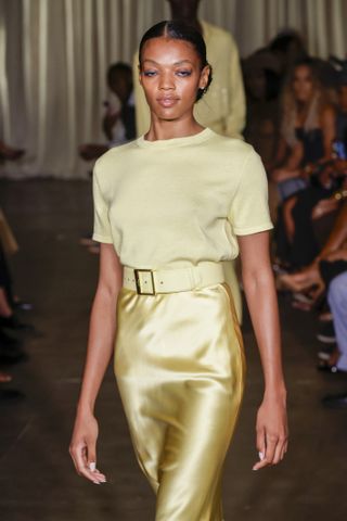 A closeup of a model walking the runway in a yellow Sergio Hudson knit top and a gold slip skirt.