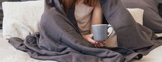 WOMAN WITH RED HAIR HOLDING A CUP IN A GREY WEIGHTED BLANKET