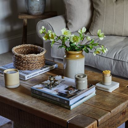 A living room with a rustic wooden coffee table styled with coffee table books, a vase of flowers and a scented candle from Pott with matching matchsticks