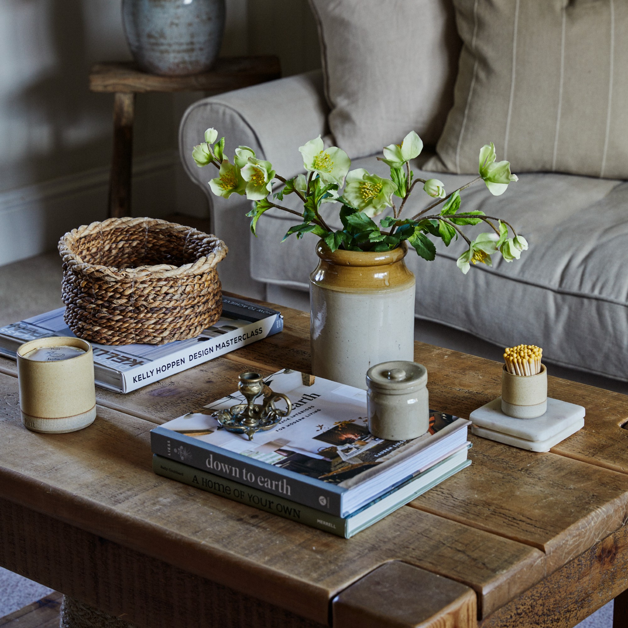 A living room with a rustic wooden coffee table styled with coffee table books, a vase of flowers and a scented candle from Pott with matching matchsticks
