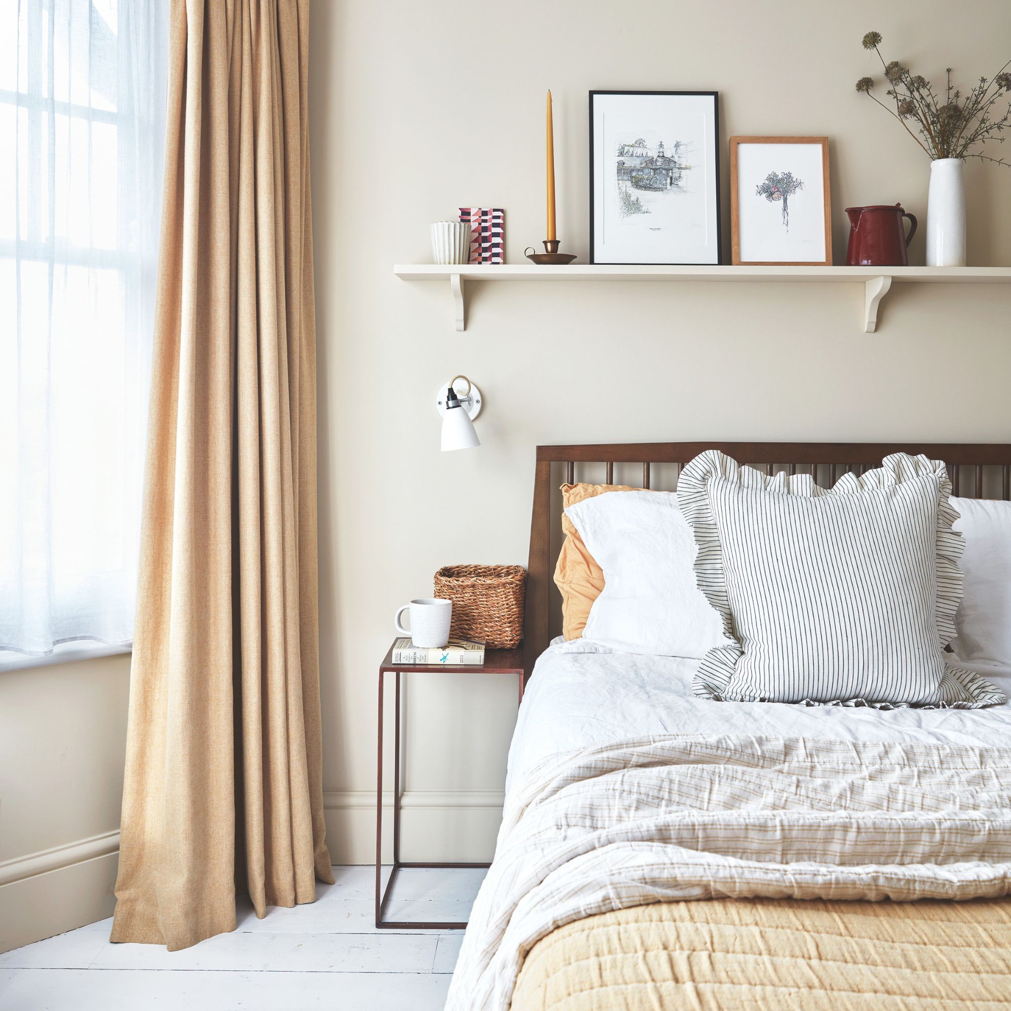 Neutral bedroom with a bed on the left and a window and cream curtain to the right and a shelf above the bed