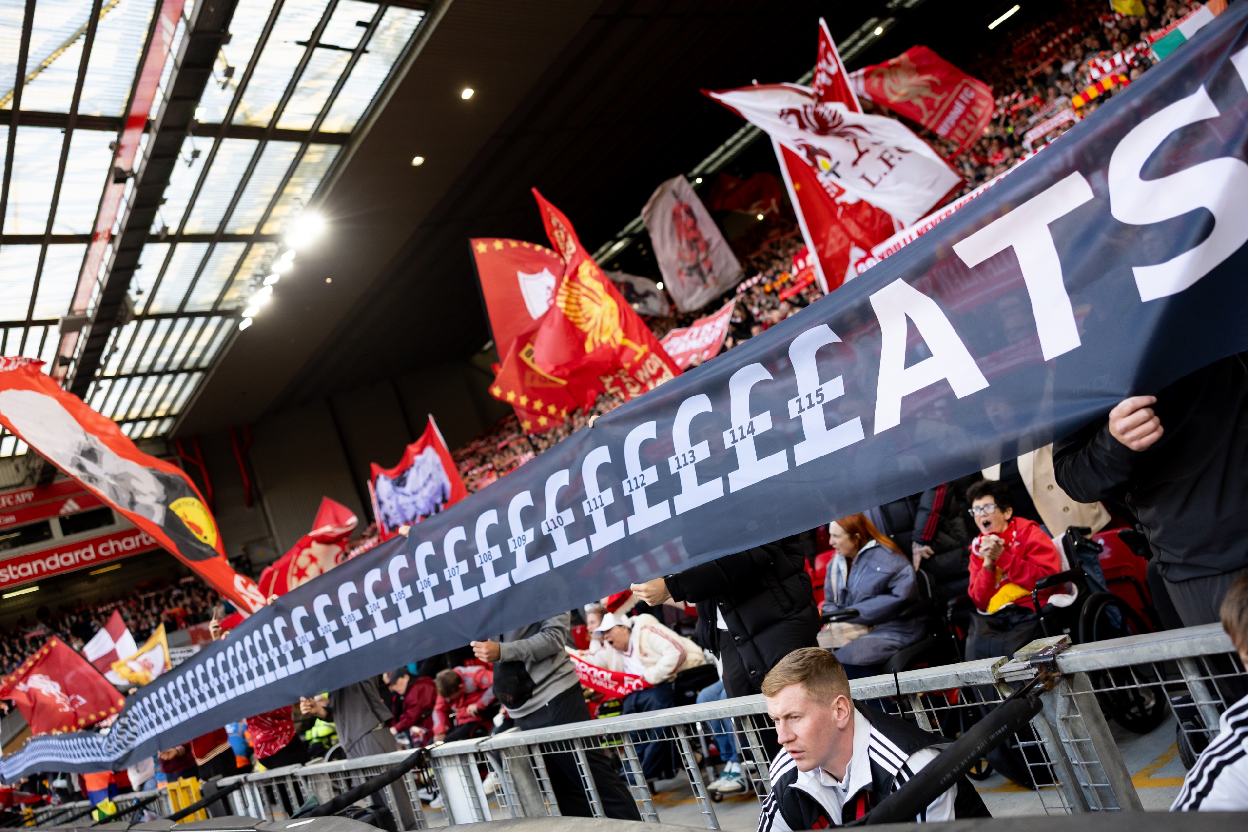Liverpool fans hold up a banner mocking Manchester City's financial scandal as the television crew work pitch-side