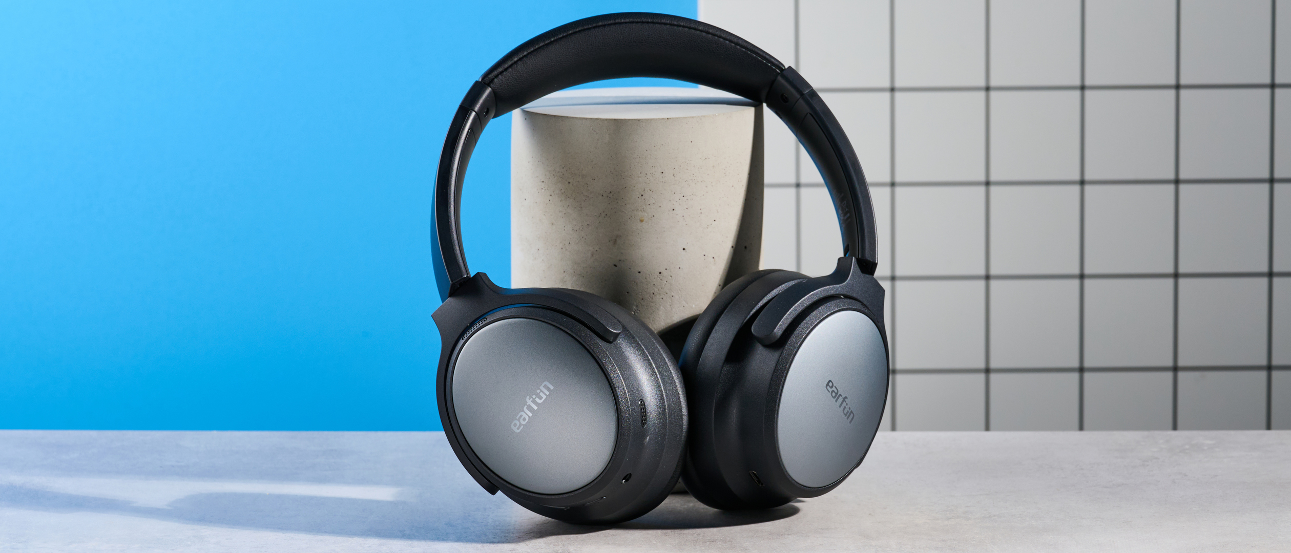 the earfun tune pro headphones, in black, with soft pleather cups, and gray cups, photographed against a blue background