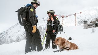 Two ski patrollers and a golden retriever in the snow