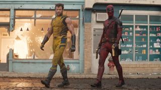 Wolverine in a yellow and blue sleeveless outfit walks next to deadpool, in a red and black outfit covering his entire body infront of an explosion in a shop.