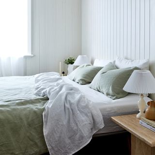 A white panelled bedroom with a bed dressed in pale sage green and white linen bedding