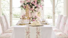 White table with pink floral dining chairs, a pink bow table runner, and gold chargers