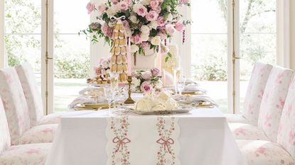 White table with pink floral dining chairs, a pink bow table runner, and gold chargers