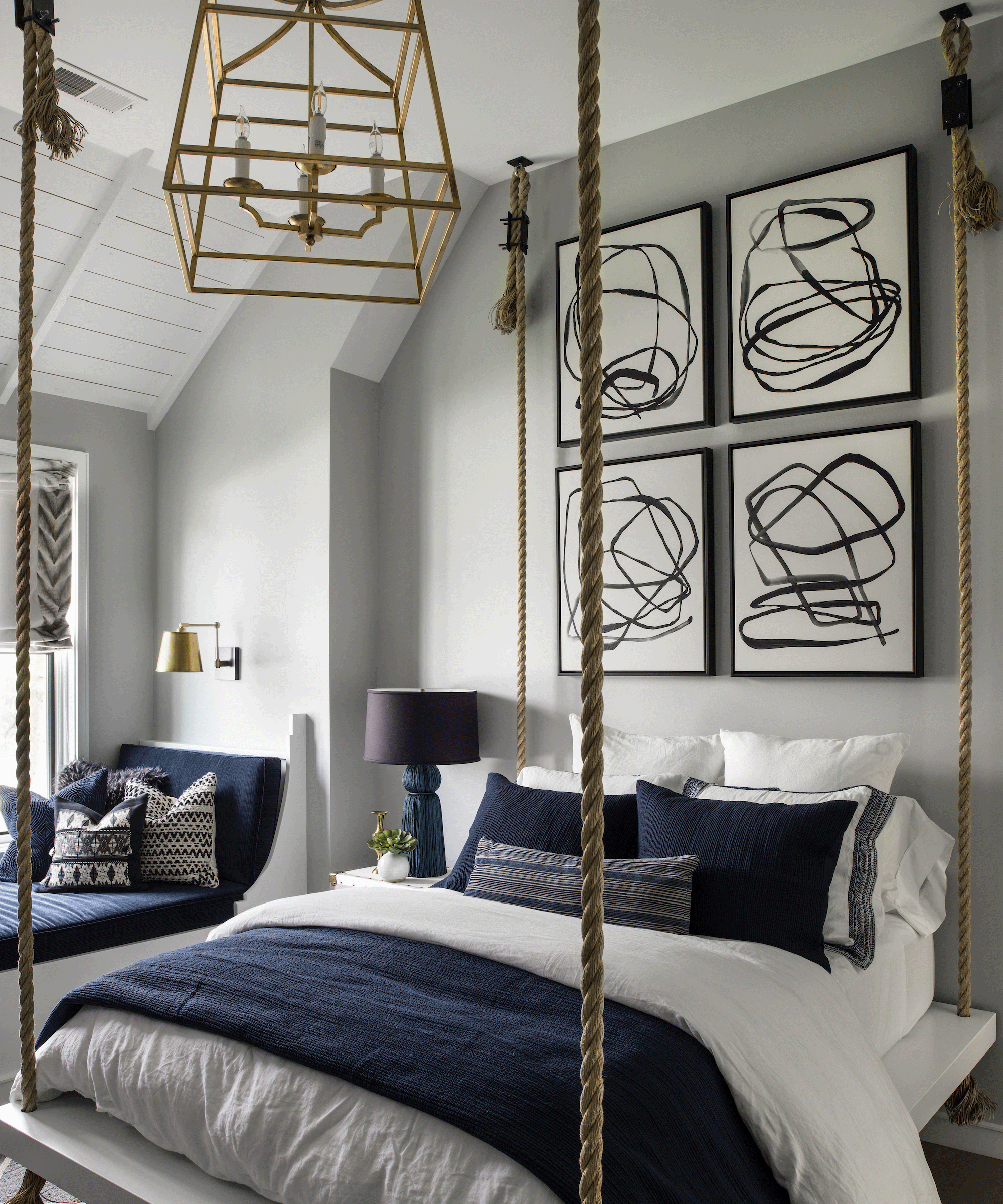 Bedroom with four poster bed with grey walls and navy bedding alongside artwork