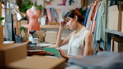 Woman sitting in a small business office, at a desk with shipping boxes, looking at her computer