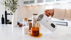 One of the best nut milk makers, the Nutr in white pouring nut milk into a mug with a carafe of nutmilk on the countertop beside it