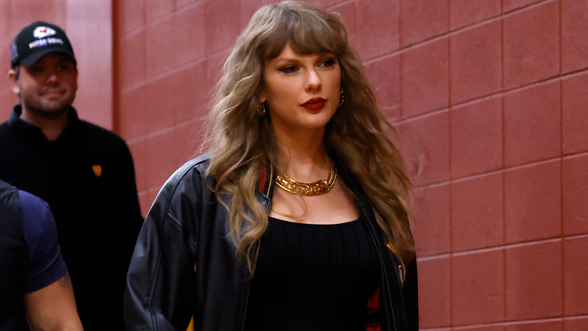 Taylor Swift walking into Arrowhead Stadium wearing a leather jacket and gold chain