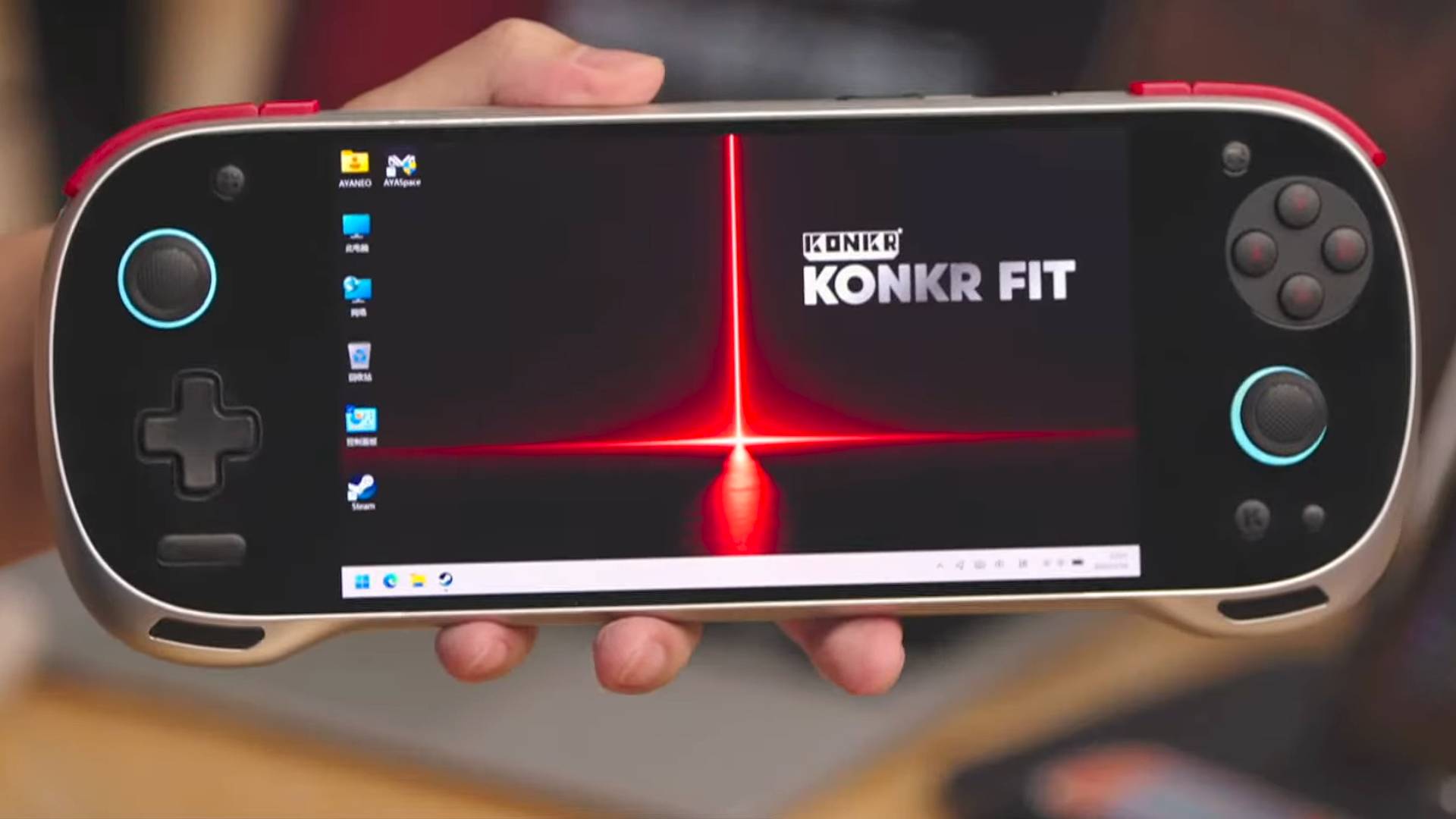 Hand holding new Ayaneo Konkr Fit handheld with branded desktop on display featuring red beam of light and product logo.