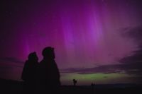 The silohettes of two people on a dazzling purple and green sky filled with auroras