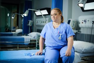 Casualty nurse Robyn Miller sitting on a hospital bed looking troubled.