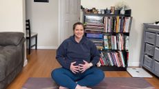 woman sits cross-legged on yoga mat doing breathing exercises