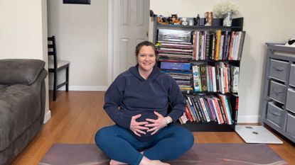 woman sits cross-legged on yoga mat doing breathing exercises