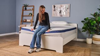 A tester sits on the edge of the mattress to test the sturdiness of the foot of the bed.