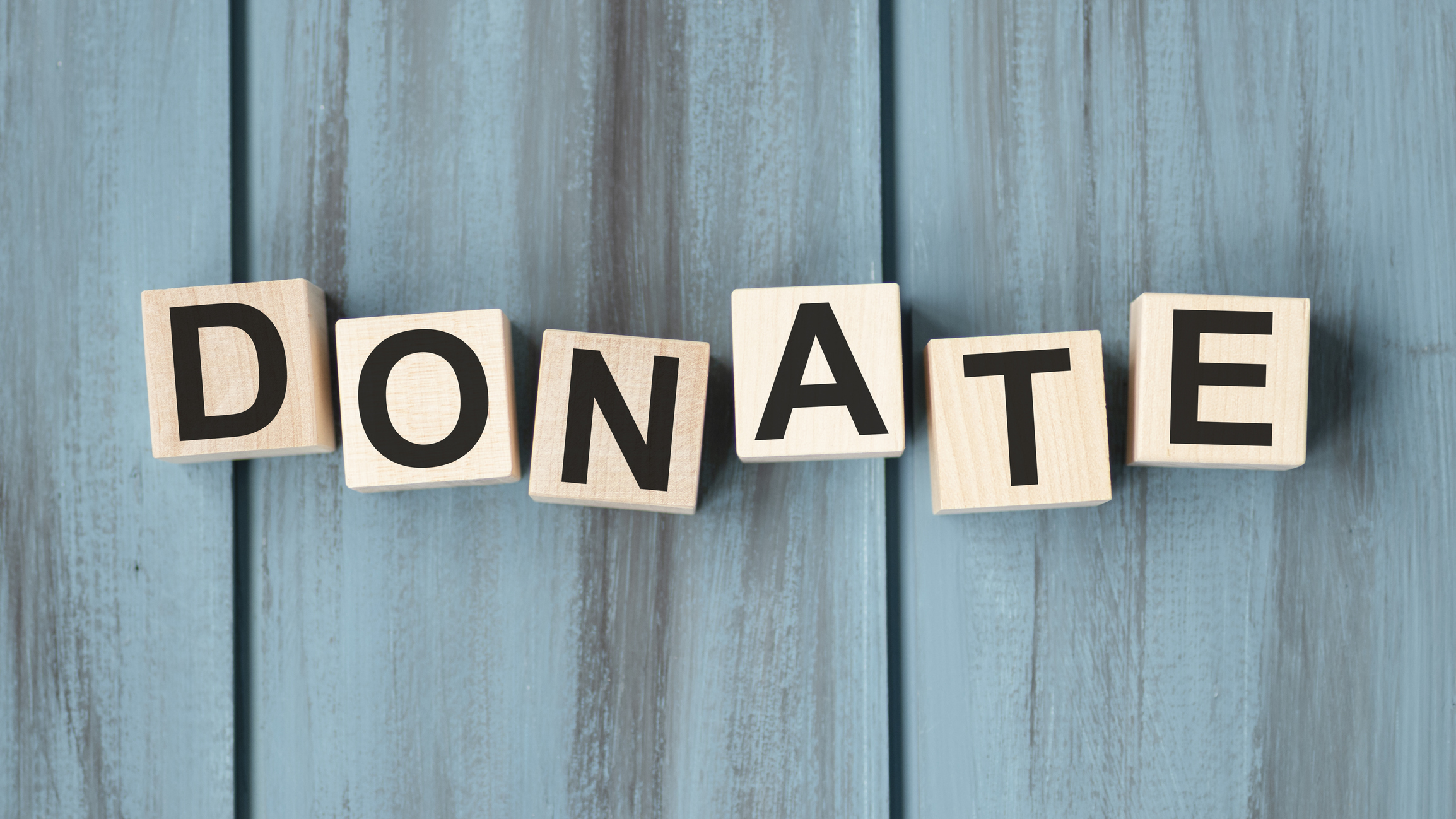 wooden blocks that spell &quot;donate&quot; on a blue weathered wood background