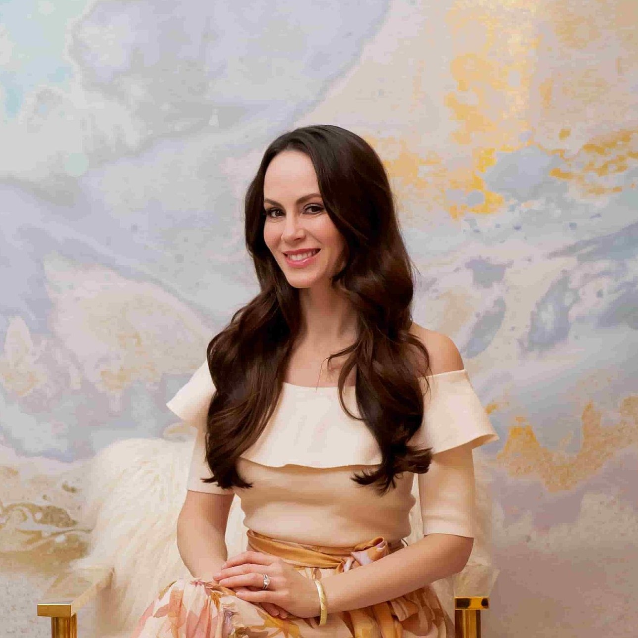 A woman with long brown hair, Lisa Chevalier, sits in front of a watercolor background and smiles.