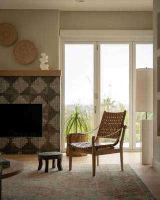 Neutral living room with tiled fireplace in diamond pattern design, faded antique rug and woven leather armchair