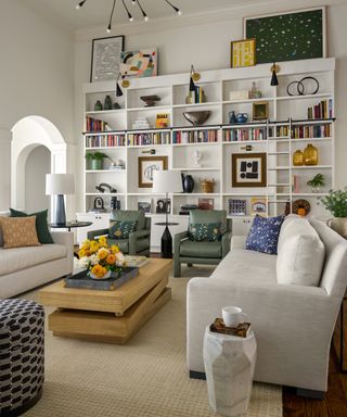 Living room with two neutral sofas and two armchairs with two legs on an area rug, and tall shelving on one wall