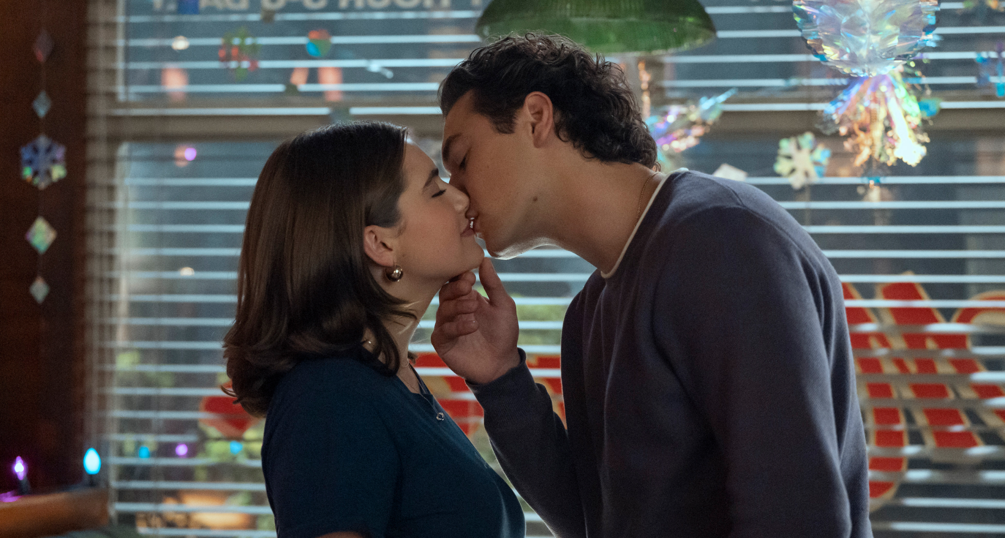Ella Bright as Hannah Wells and Belmont Cameli as Garrett Graham kissing in a diner with snowflake stickers on the windows
