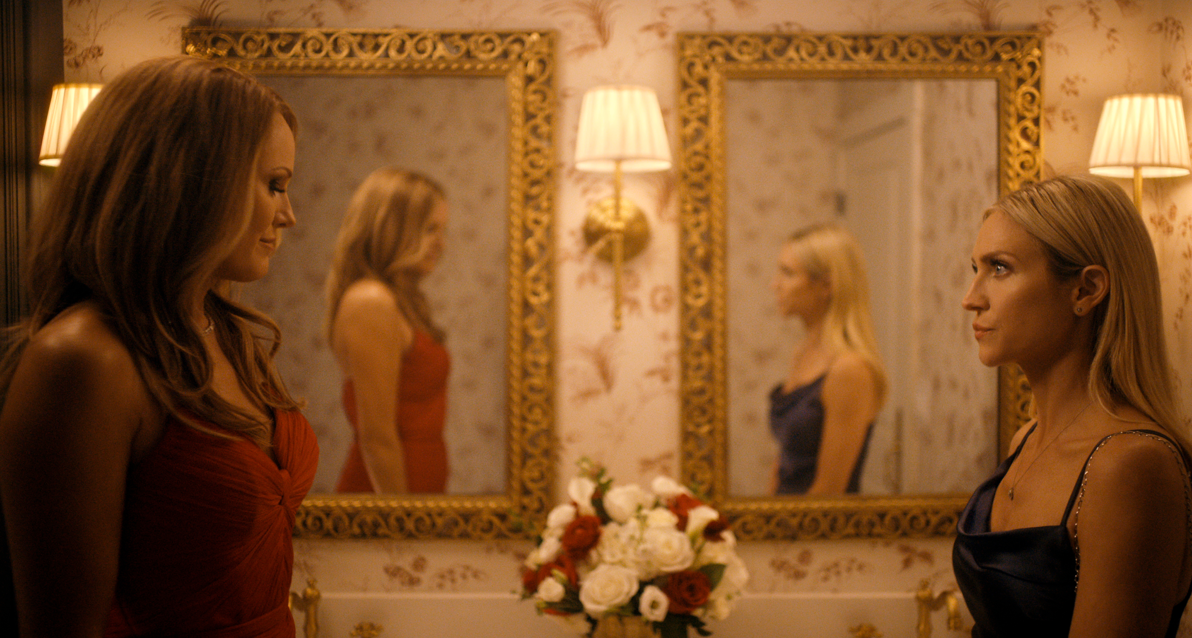 malin akerman and brittany snow look at each other while standing in front of a lavish bathroom mirror in the hunting wives season 2