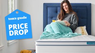 A woman sitting on a Linenspa Dreamer 8-inch Hybrid Mattress wrapped in a blue blanket, a Tom's Guide price drop deals graphic (left)