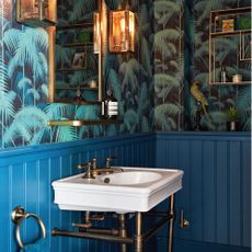 Cloakroom, hand basin, shelves and lantern lights, with vivid patterned blue wallpaper and tongue and groove woodwork. 