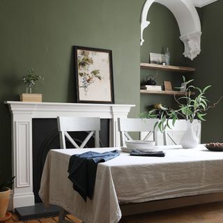 A dark green-painted dining room with a white fireplace and architectural features and a long rectangular table