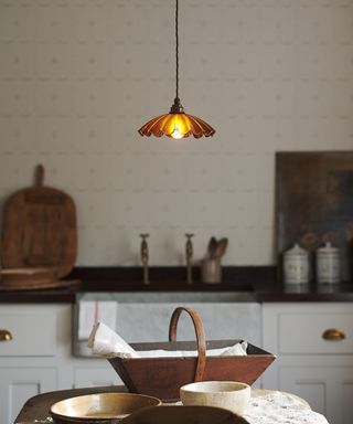 low hanging small amber coloured glass frilled light above kitchen island with wooden trug and bowls on top of island