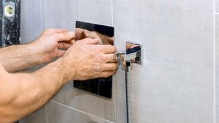 Arms fitting a chrome shower on grey tiles