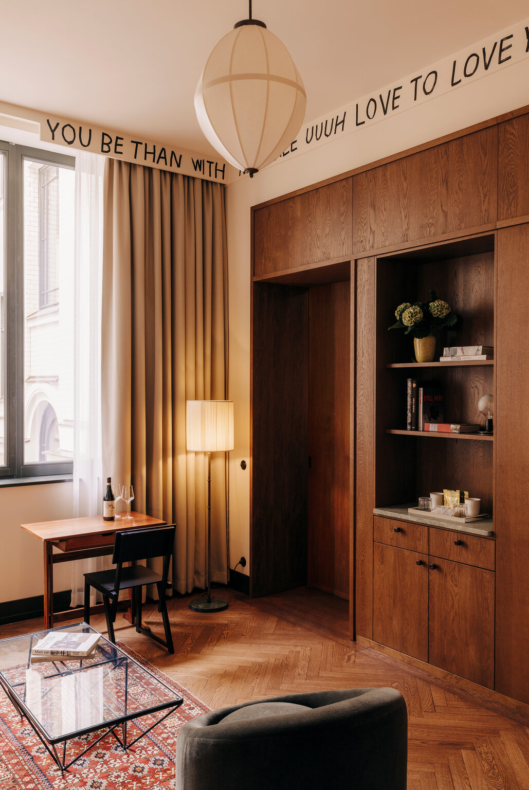 A woody hotel lobby with curated collectibles on shelves, warm lighting, red moroccan rugs, velvety furniture, and beige curtains.