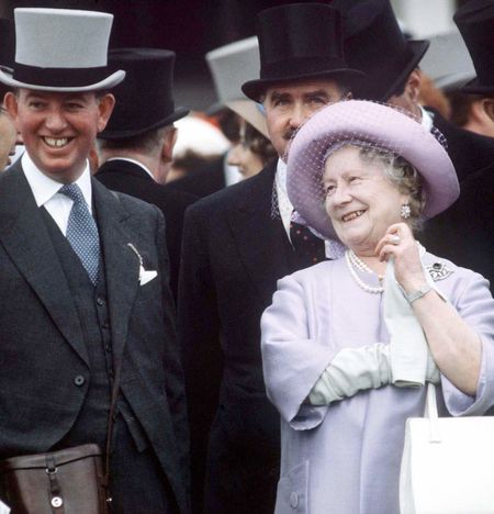 The Queen Mother wearing a lavender coat and hat laughing next to Prince Philip and men in top hats