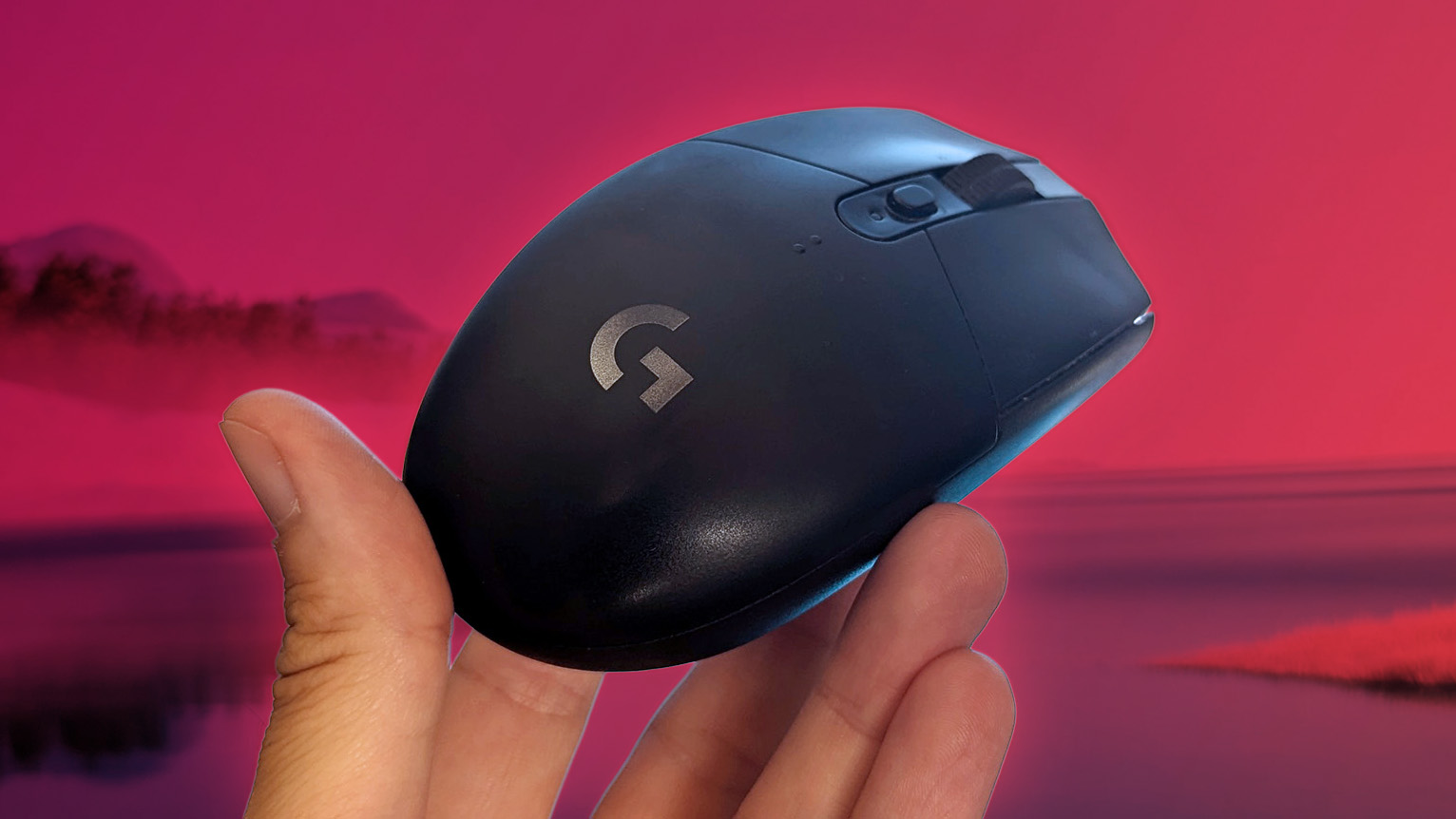 Logitech G305 LIGHTSPEED wireless gaming mouse held in hand in front of a pink background scene