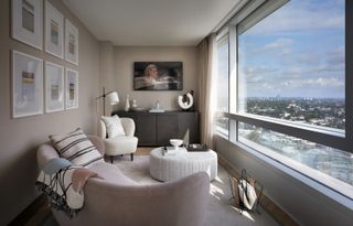 A living room in an apartment with a large window with views of the city, and a curved pink sofa and boucle armchair